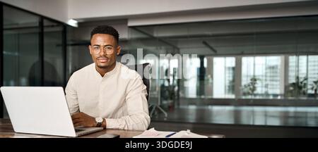 Confident professional African business man looking at camera using computer. Stock Photo