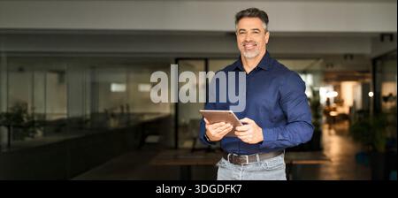 Smiling mature business man executive standing in office with tablet. Portrait Stock Photo