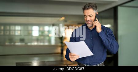 Happy busy mature older business man manager holding papers making call at work. Stock Photo