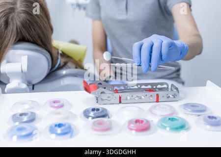 Gloved dental professional holds mirror and probe near child in dental chair with instruments and supplies on clinic table Stock Photo