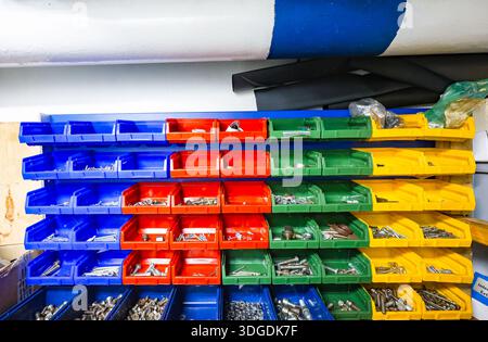 Colorful plastic storage bins with bolts, screws and metal fasteners organized on shelves in an industrial workshop or warehouse Stock Photo
