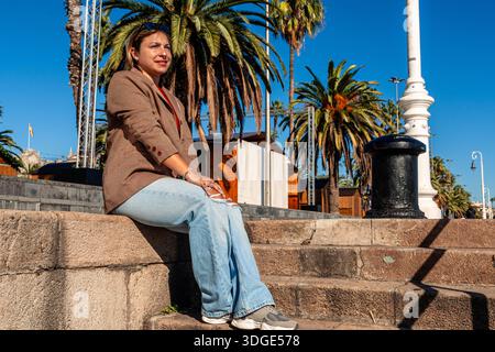 Woman relaxing on stairs in port of barcelona with palm trees Stock Photo