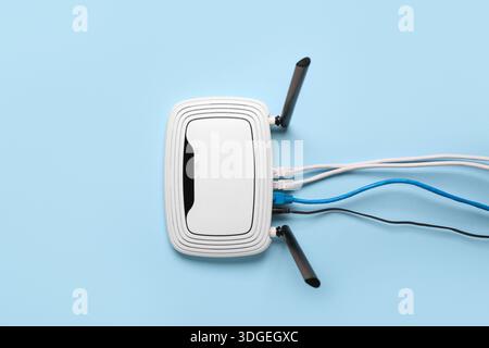 Modern wi-fi router with cables on blue background Stock Photo