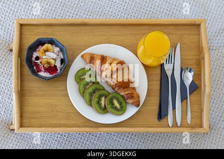 Top view of breakfast tray with croissant, kiwi slices, yogurt bowl, juice and cutlery Stock Photo