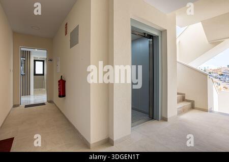 Clean indoor hallway in residential building featuring open elevator, tiled floor and natural lighting Stock Photo