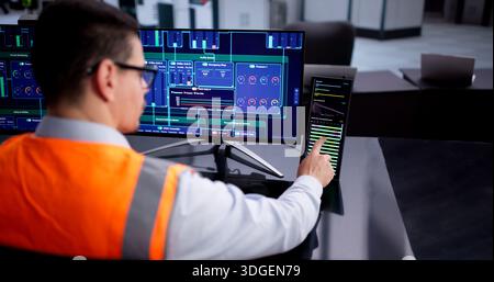 Young Hispanic Male Using Industrial SCADA Software In Semiconductor Factory. Stock Photo