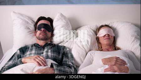 Interior Designer Couple Sleeping Peacefully With Eye Masks On Bed Stock Photo