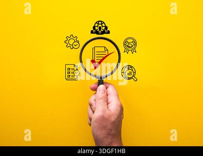 Hand holding a magnifying glass highlighting a document with a red checkmark on a yellow background Stock Photo