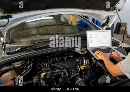 Auto mechanic performing car diagnostics using laptop under open hood Stock Photo