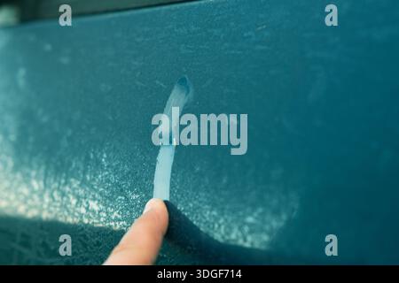 Finger defrosting frosted ice on car window during spring thaw Stock Photo