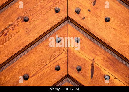 Close-up of a rustic wooden door with a chevron pattern and wrought iron studs. Traditional carpentry and vintage architectural detail Stock Photo