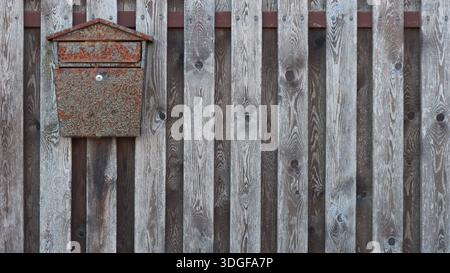 Old metal mailbox with a touch of rust hanging on the textured planks of a rustic fence, retro postal composition with a mail container with a wood Stock Photo