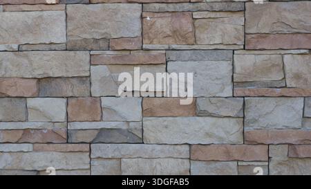 A fragment of a tiled wall made of natural stone, a mosaic of square shapes of different sizes in a gray-brown color scheme, decorative stone finish Stock Photo