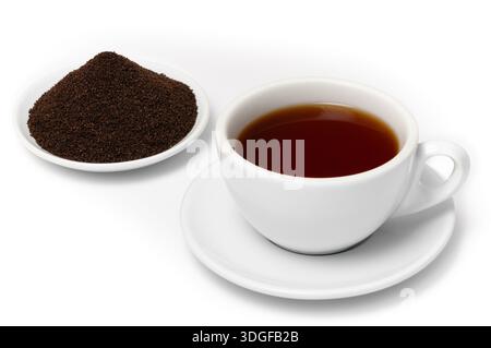 White cup of freshly brewed Ceylon Dimbula Broken Orange Pekoe Fannings tea on saucer with pile of dried black tea fannings on plate, isolated on whit Stock Photo