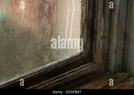 Condensation and water droplets on a misty window pane in an old wooden frame with peeling paint. Stock Photo