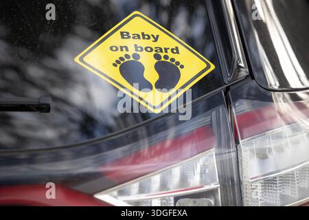 Close-up of a yellow "Baby on board" warning sticker on the rear window of a car. The sign features black text and an icon of two footprints. Stock Photo