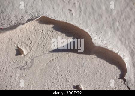 Macro photo of a defect on a plastered drywall surface. The top layer of acrylic vinyl-based paint is peeling, revealing the texture of the wall and c Stock Photo