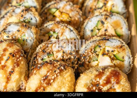 Close-up of crispy fried sushi rolls topped with sesame and sauce. Detailed texture and visible fillings emphasize crunchy Asian fusion street food. Stock Photo