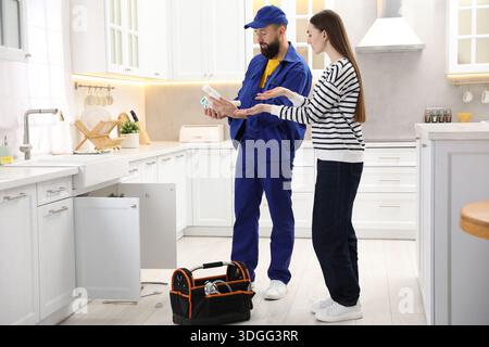 Woman and plumber looking at drainage pipe and siphon in kitchen Stock Photo