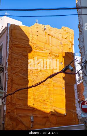 The textured orange facade of a building covered in polyurethane spray foam insulation during renovation. An abstract urban detail against a clear blu Stock Photo