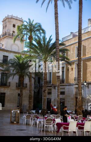 Alicante, Spain – Nov 14, 2021: Waiters preparing outdoor cafe tables with red tablecloths on Santisima Faz square, surrounded by historic architectur Stock Photo