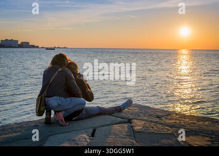 Couple hugging, rear view of a couple on vacation watching a scenic sunset over the Adriatic Sea, Trieste, Italy Stock Photo