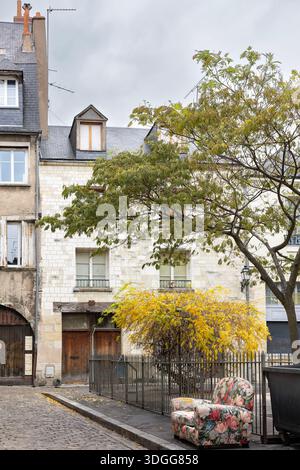 Old floral sofa furniture stands on cobblestone street near trash bin and yellow autumn trees in front of historic building in Tours France creating a Stock Photo