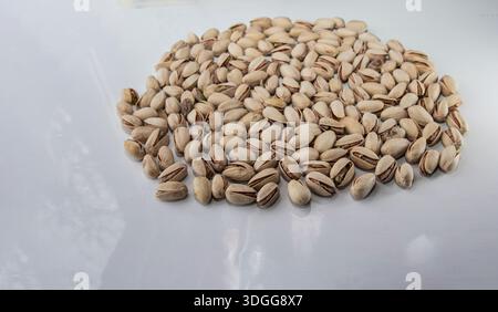 Pistachio nuts in shells scattered on white surface for food background use Stock Photo