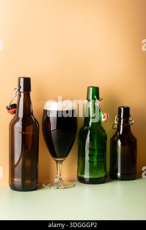 Glass of dark beer with foam head and empty bottles on colorful green and orange background, bright shadows Stock Photo