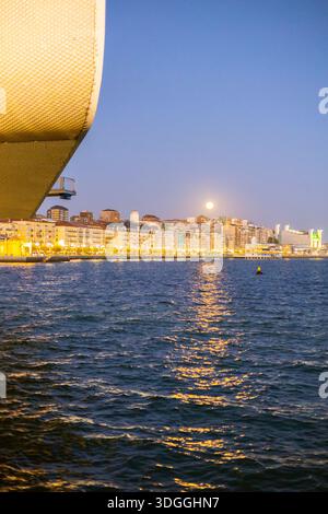 SANTANDER, SPAIN – NOV 19, 2021: Vertical shot of the moon rising over Santander city illuminated buildings with the textured facade of Centro Botin a Stock Photo