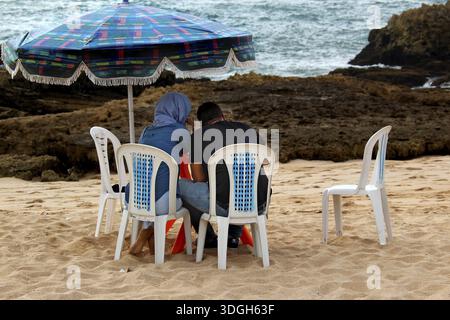 Two people sitting under a colorful sunshade on the beach in Oulidia, Oulidia, Morocco Stock Photo
