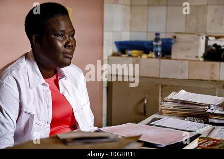 Nurse sitting seriously at desk surrounded by files and documents, Bouke, region, Cote d'Ivoire Stock Photo