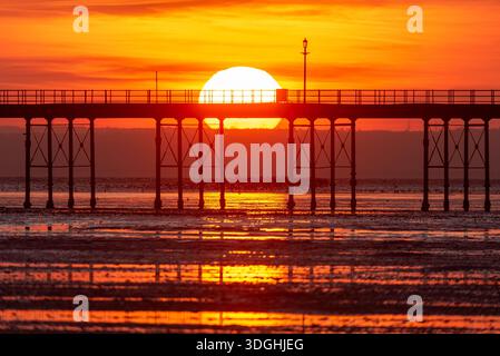 Solar disk setting sun going down behind the iron structure of Southend Pier, Southend on Sea, Essex, UK. Last day of 2025. Flock of birds passing low Stock Photo