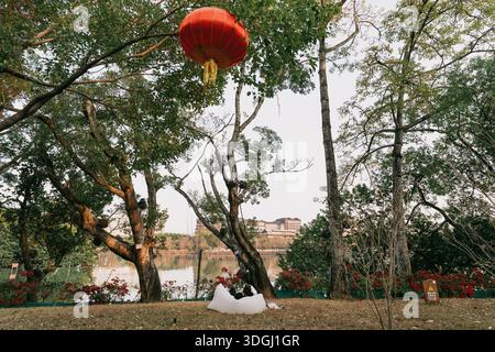 Red lantern hanging in a park with trees and a couple sitting on a blanket - West Lake in Huizhou, Guangdong Province, China, is a tourist attraction featuring ancient architecture Stock Photo