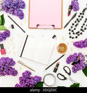 Creative flat lay with lilac flowers, stationery and makeup on white background, spring feminine workspace Stock Photo