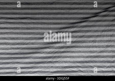 Front view of wrinkled and striped tarp in black and white. Abstract high resolution full frame textured background. Stock Photo