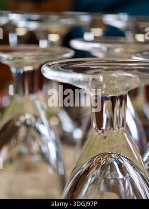 Clear glass wine goblets set upside down in a neat row on a table, sparkling with reflections and soft bokeh lights, ready for service in a bar or cat Stock Photo