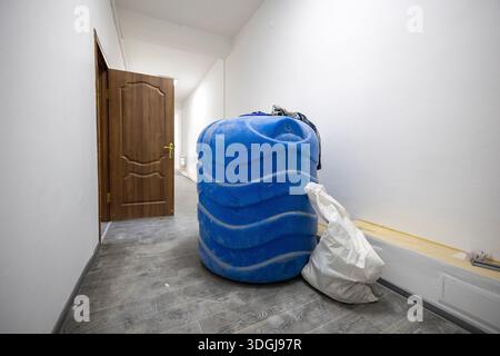 A large blue plastic water tank and a sack sit in a hallway during home renovation. This highlights the practical realities of construction and the ne Stock Photo