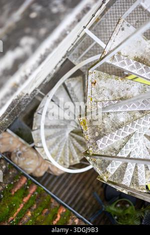 A high-angle view of a weathered, outdoor metal spiral staircase. The diamond plate steps provide an industrial texture. A concept of utilitarian arch Stock Photo