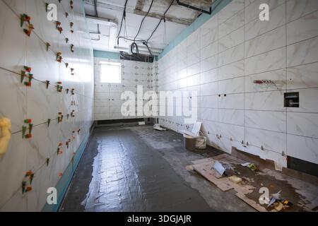 A large bathroom under renovation, with new ceramic tiles on the walls using plastic spacers. The wet screed covers a newly installed underfloor heati Stock Photo