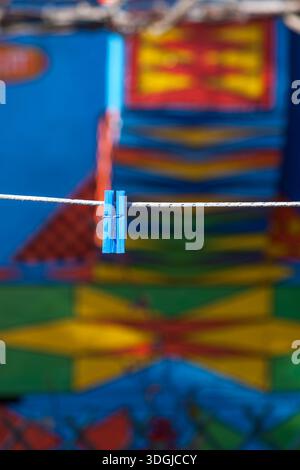 Two blue clothespins on a clothesline, with a vibrant, colorful mural blurred in the background. A concept of daily chores and the simple beauty found Stock Photo