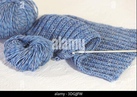 A scarf crochet project in blue wool shown with crochet hook against a white background. Stock Photo