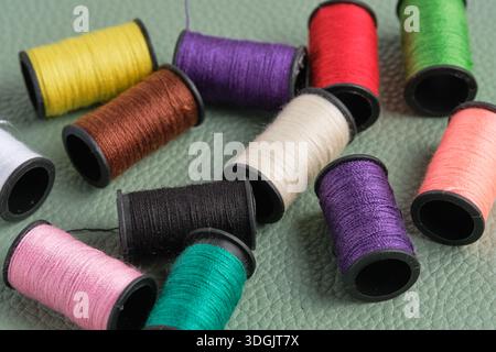 Spools of multicolored sewing threads on green leather background Stock Photo