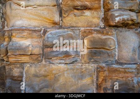 High-resolution texture of a weathered sandstone wall showing beautiful orange, tan, and grey mineral banding. Stock Photo