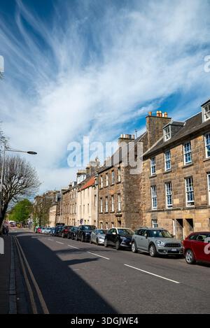 Perspective view of a historic street in St. Andrews lined with classic stone buildings, parked cars, and wispy cirrus clouds. Stock Photo