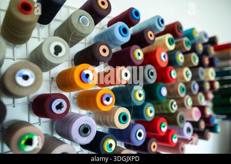 Spools of thread of various colors neatly arranged on wooden shelves, creating a visually appealing display for sewing and tailoring projects or facil Stock Photo