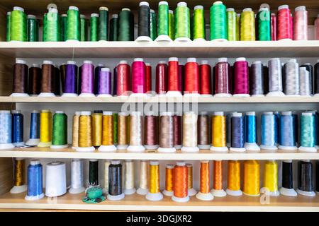 Spools of thread of various colors neatly arranged on wooden shelves, creating a visually appealing display for sewing and tailoring projects or facil Stock Photo