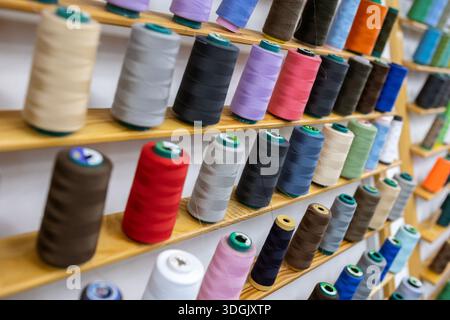 Spools of thread of various colors neatly arranged on wooden shelves, creating a visually appealing display for sewing and tailoring projects or facil Stock Photo