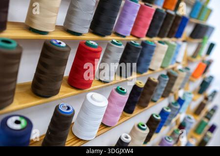Spools of thread of various colors neatly arranged on wooden shelves, creating a visually appealing display for sewing and tailoring projects or facil Stock Photo