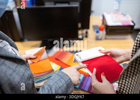 Two designers or a client and a decorator collaborating on a project. They are choosing from a variety of colorful fabric swatches for fashion or inte Stock Photo